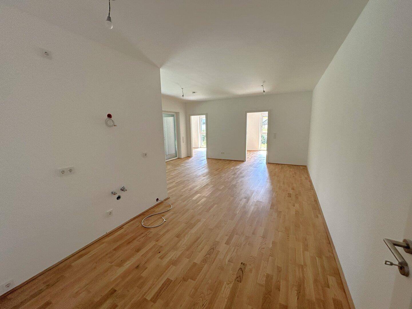 Heller Wohnbereich mit Holzboden und mehreren Türöffnungen, ideal für offene Wohnkonzepte.