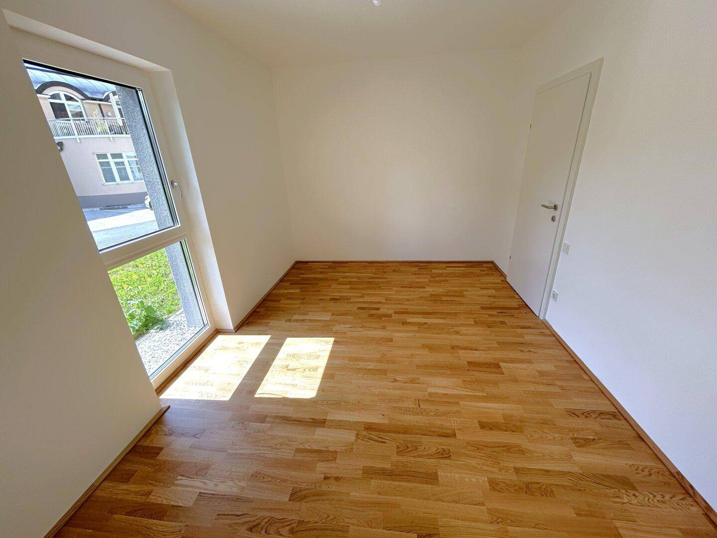 Sonniger Raum mit Holzboden und großem, schrägem Fenster, das viel Tageslicht hereinlässt.