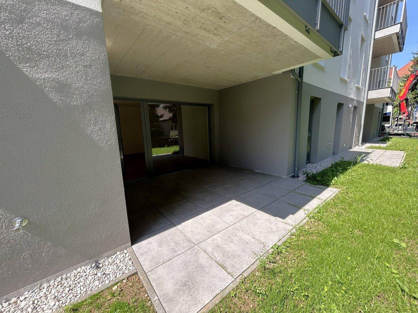 Ebenerdige Terrasse mit grauen Fliesen und direktem Zugang zum grünen Gartenbereich des Neubaus.