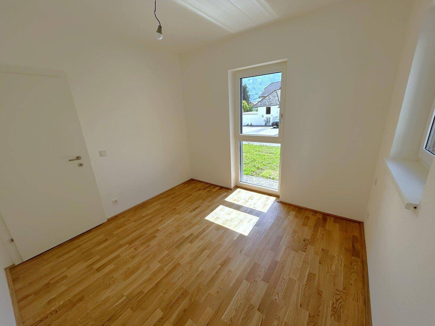 Helles Schlafzimmer mit Holzboden und einem Fenster, das viel Tageslicht hereinlässt.