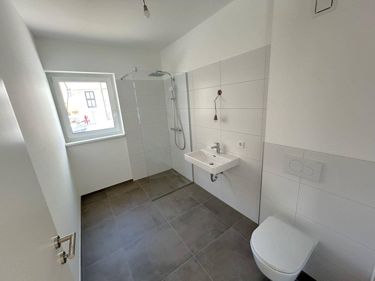 Modernes Badezimmer mit ebenerdiger Dusche, Waschbecken, wandhängendem WC und Fenster.