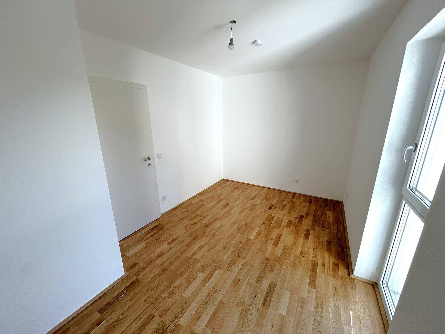 Ruhiges Zimmer mit hellem Parkettboden und einem Fenster, das für angenehme Lichtverhältnisse sorgt.