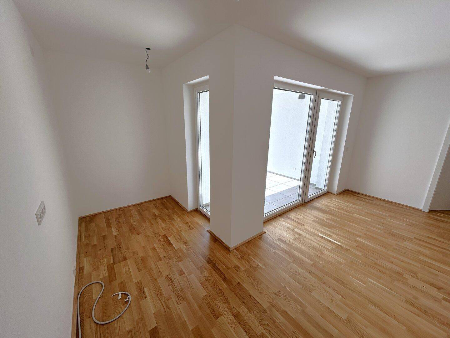 Lichtdurchflutetes Zimmer mit Parkettboden und großen Fenstern in der Ecke.