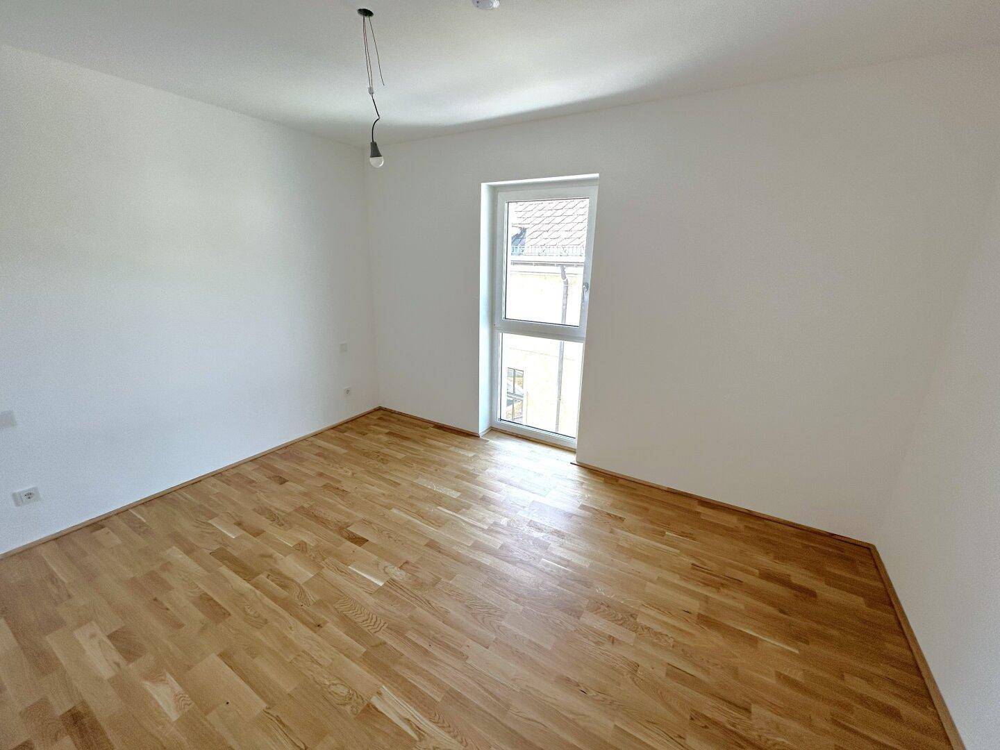 Ruhiges Schlafzimmer mit hellem Parkettboden und einem Fenster, ideal für erholsame Nächte.