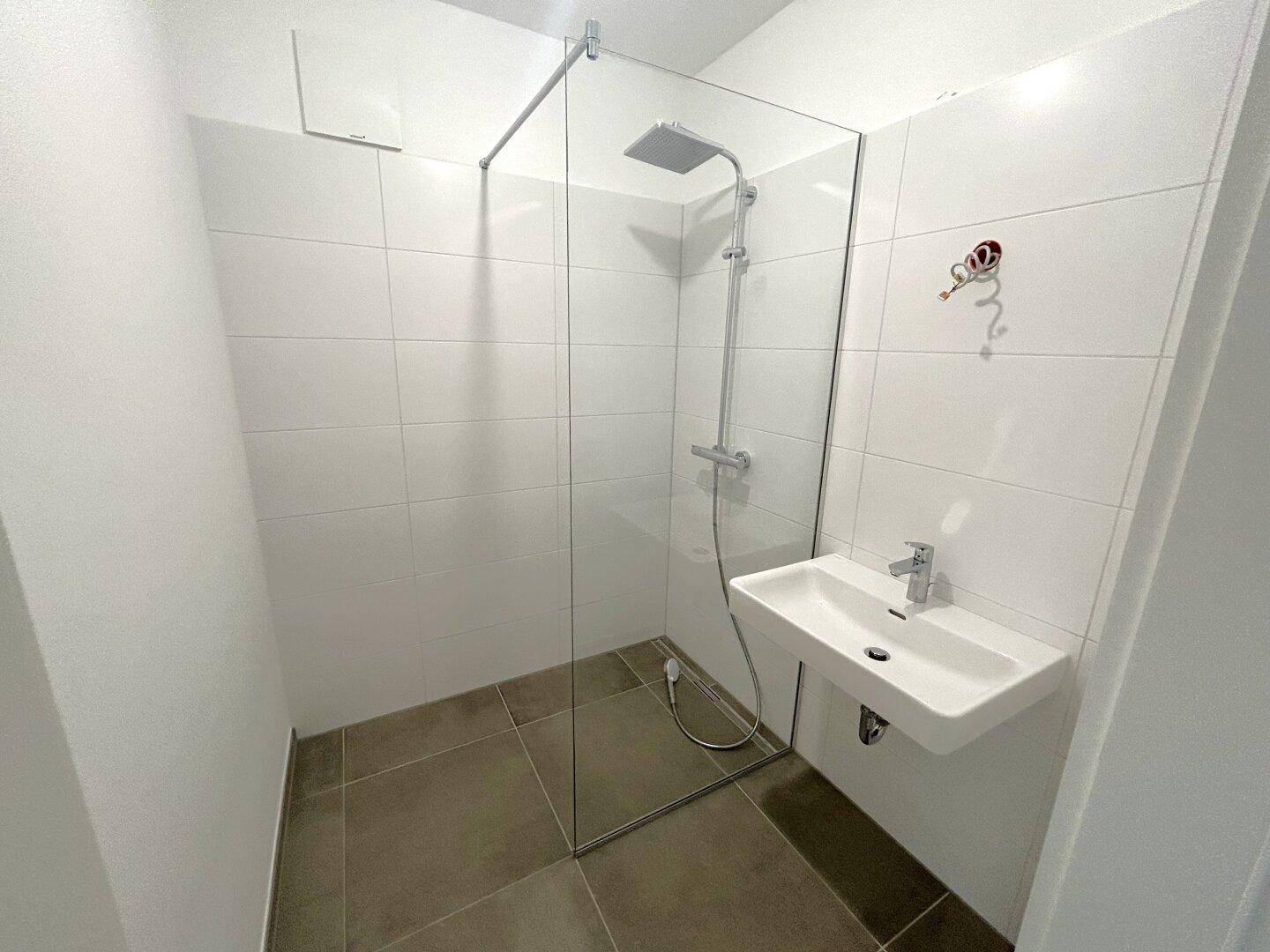 Modernes Badezimmer mit ebenerdiger Dusche, weißen Wandfliesen und einem wandhängenden Waschbecken.