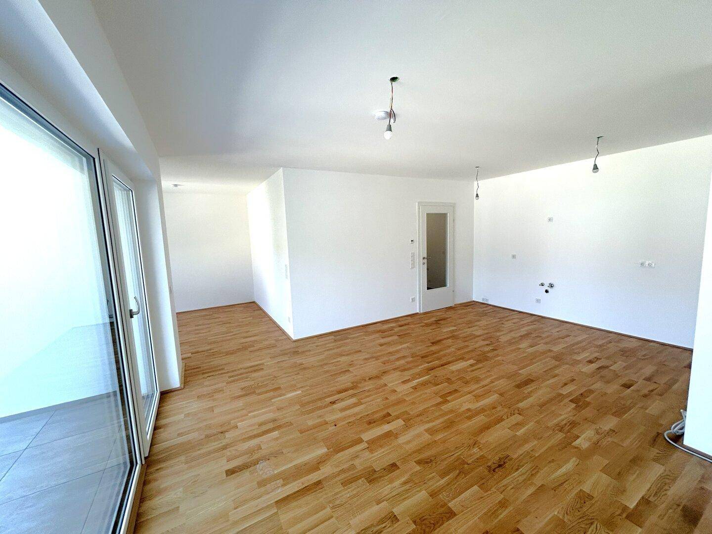 Offener Wohnbereich mit Parkettboden, weißen Wänden und viel Tageslicht.