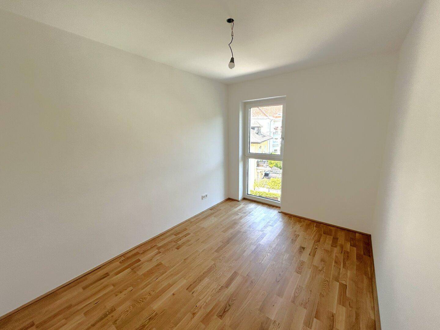 Gemütliches Zimmer mit hellem Parkettboden und einem Fenster für viel Tageslicht.
