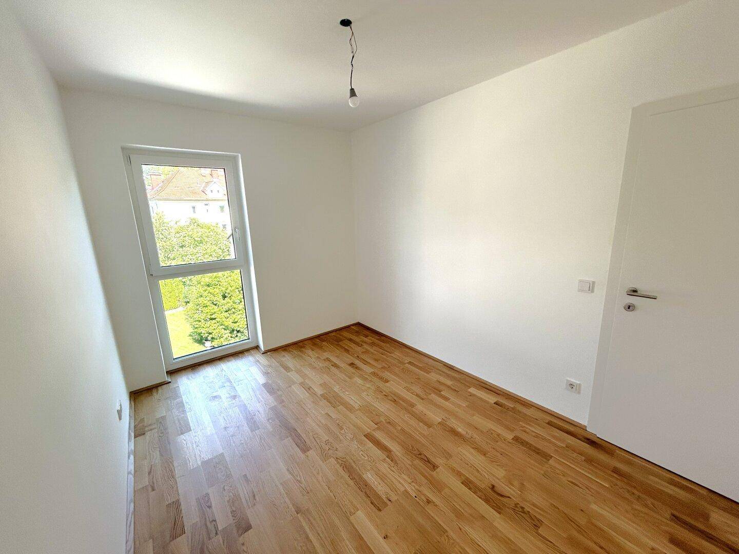 Modernes Zimmer mit Parkettboden und weißer Tür, ideal als Schlaf- oder Arbeitszimmer.
