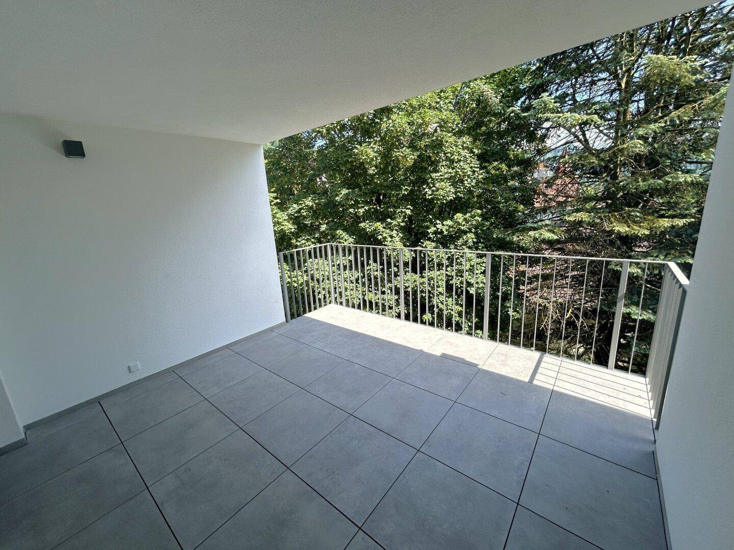 Heller Balkon mit grauen Fliesen und weitem Blick auf die umliegende Natur.
