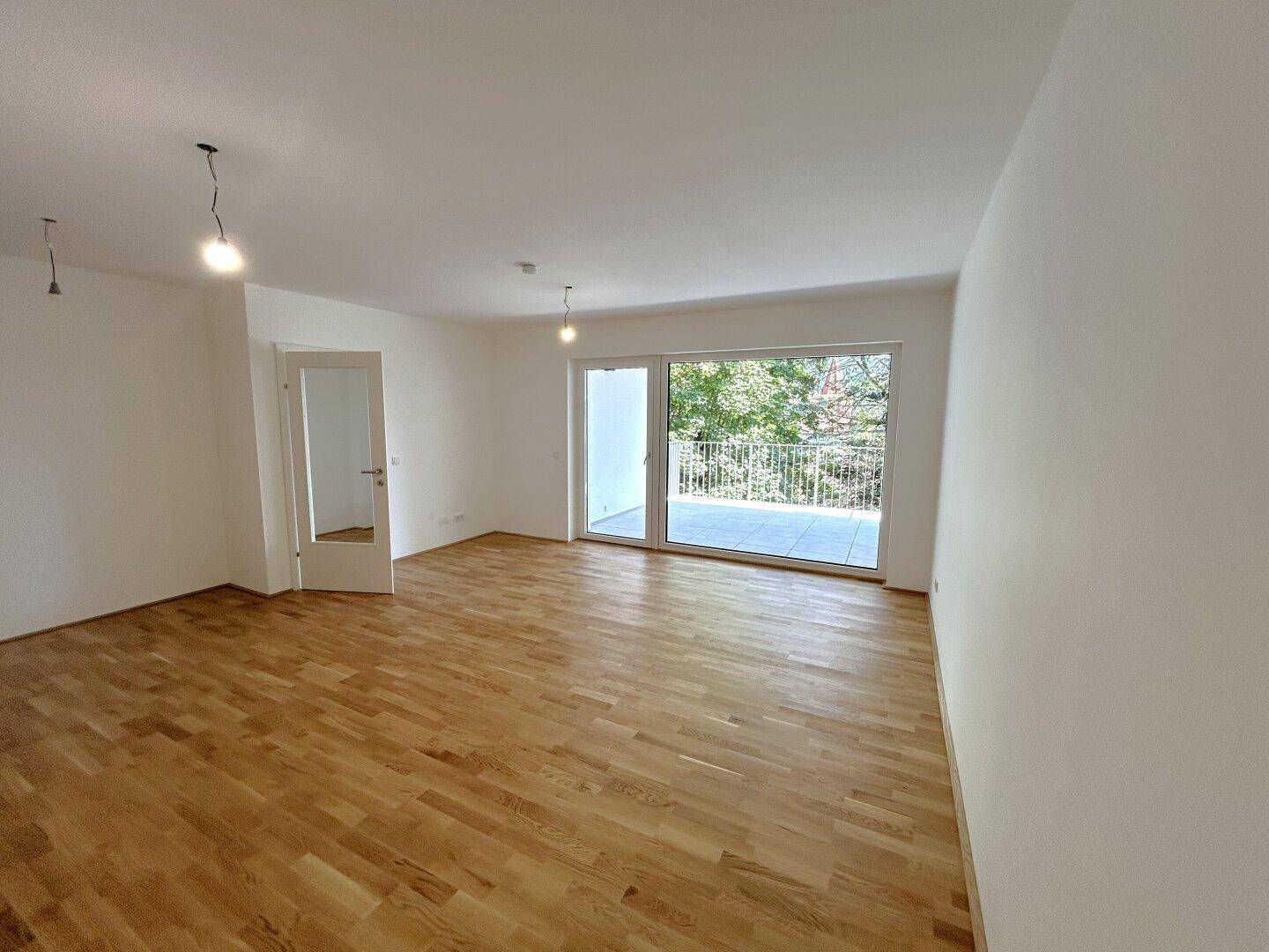 Helles Wohnzimmer mit Parkettboden und Zugang zu einem geräumigen Balkon mit Blick ins Grüne.