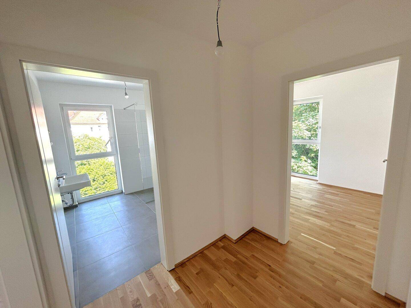 Heller Flur mit Parkettboden, der zu einem Badezimmer und einem weiteren Zimmer führt.