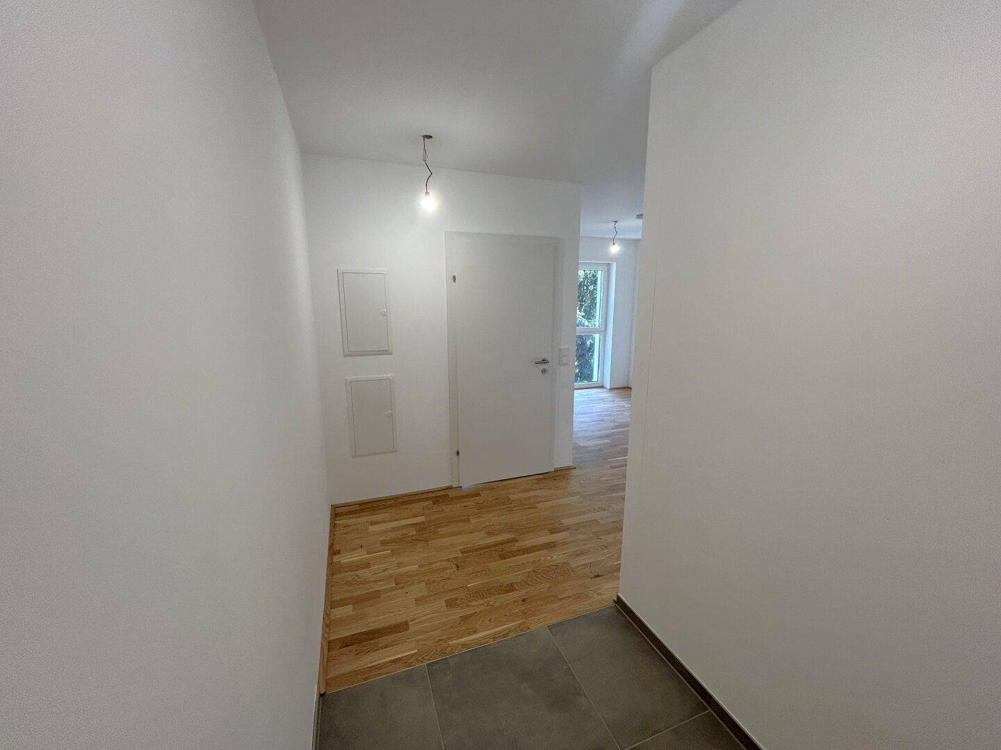 Eingangsbereich mit Fliesenboden, der in einen hellen Flur mit Holzboden übergeht.
