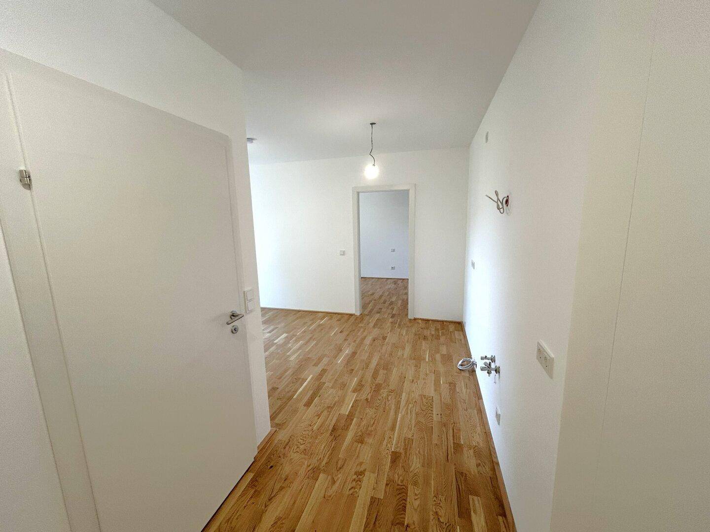 Heller Flur mit Holzboden, der zu weiteren Zimmern der Wohnung führt.
