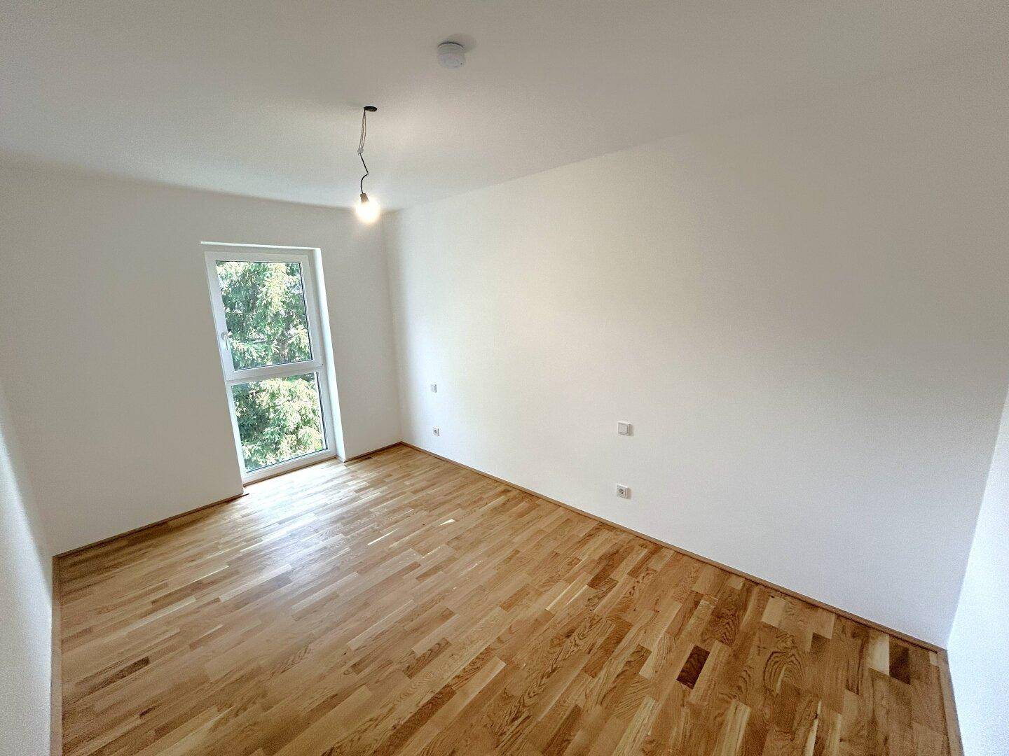 Geräumiges Zimmer mit Parkettboden und Fenster, das viel Tageslicht hereinlässt.
