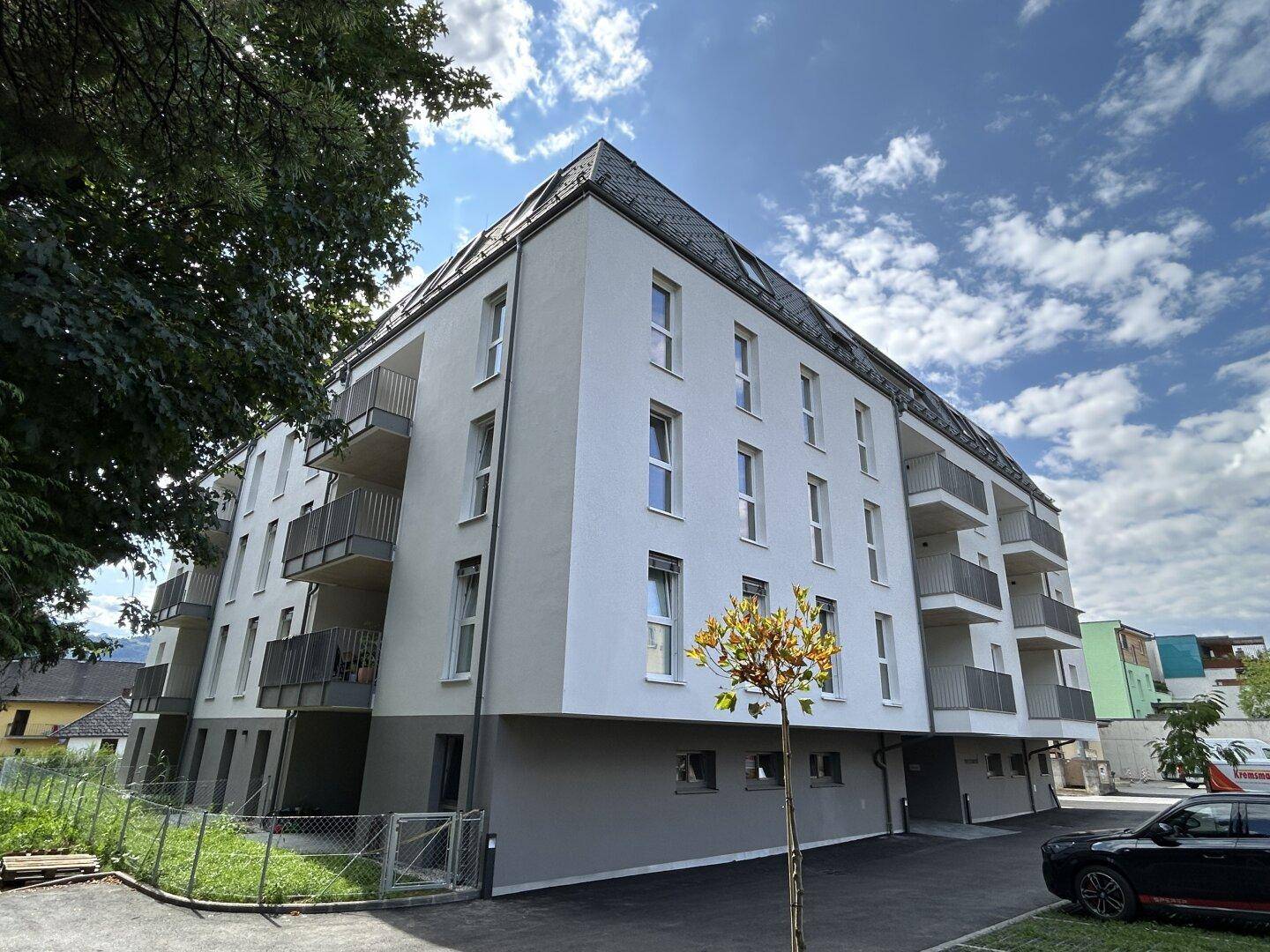 Modernes Mehrfamilienhaus mit Balkonen und Satteldach unter blauem Himmel.