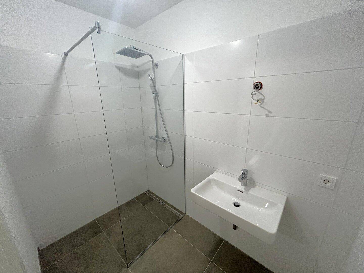 Modernes Badezimmer mit begehbarer Dusche, Regenduschkopf, wandhängendem Waschbecken und weißen Fliesen.