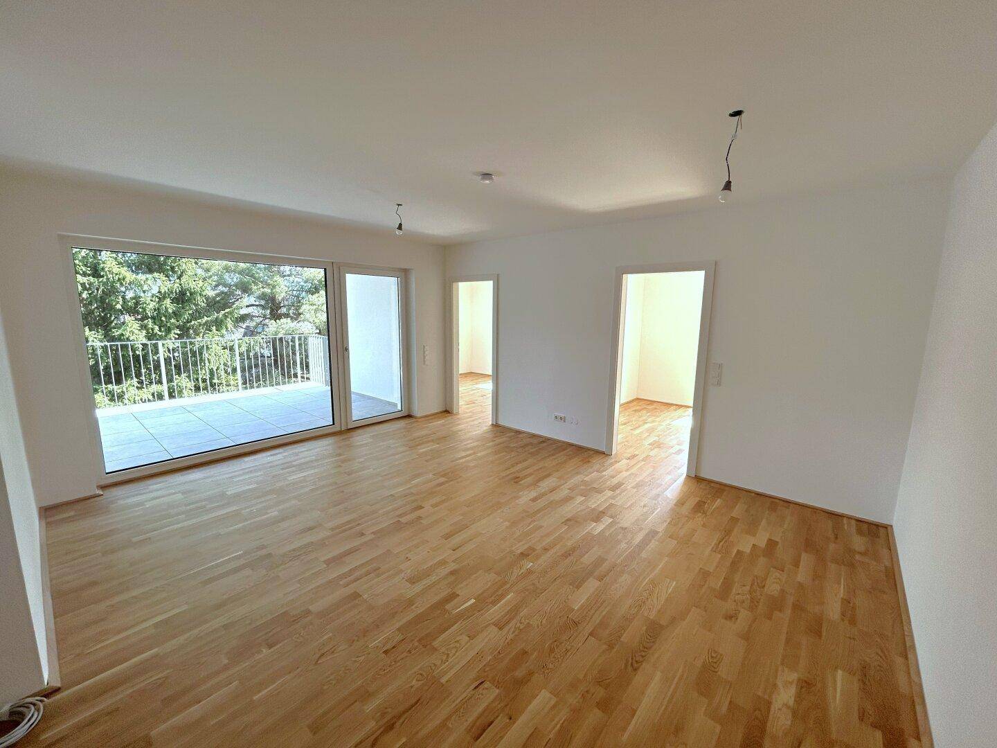 Helles Wohnzimmer mit Echtholzparkett und Zugang zu einem großen Balkon.