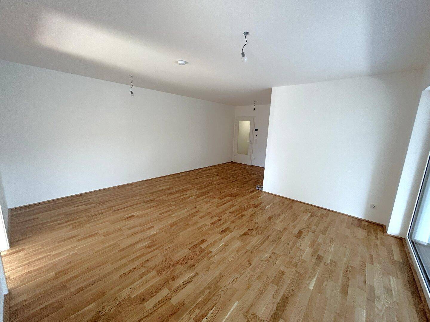 Lichtdurchflutetes Wohnzimmer mit hochwertigem Parkettboden und weiß gestrichenen Wänden.
