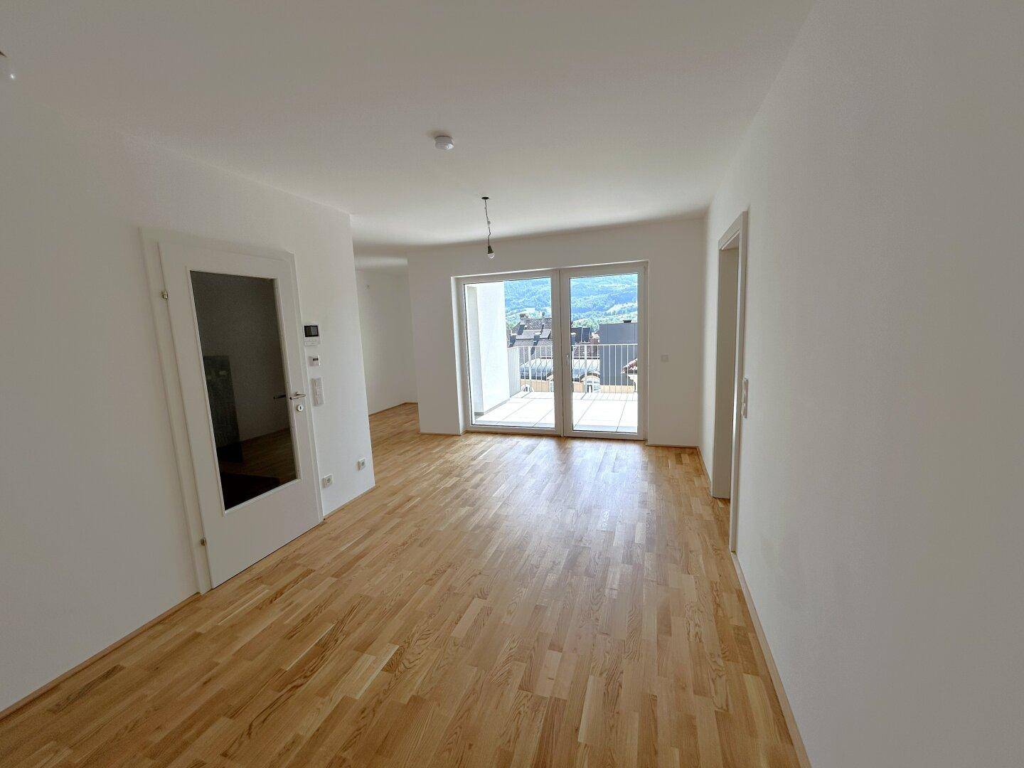 Geräumiges Zimmer mit hellem Parkettboden und Zugang zu einem Balkon mit schöner Aussicht.