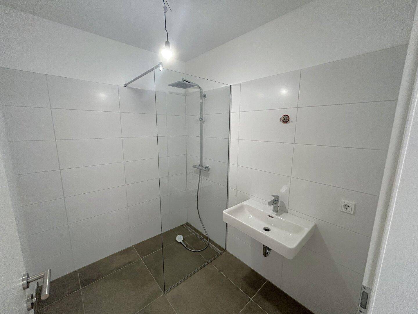 Modernes Badezimmer mit weißen Fliesen, einer begehbaren Dusche und einem Wandwaschbecken.
