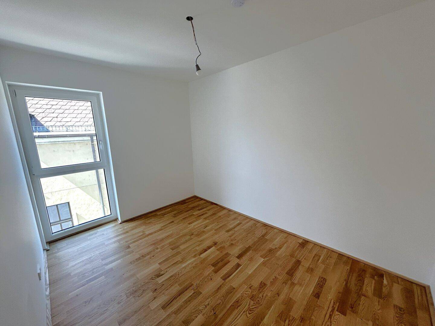 Helles Schlafzimmer mit Parkettboden und einem großen Fenster, das viel Tageslicht hereinlässt.