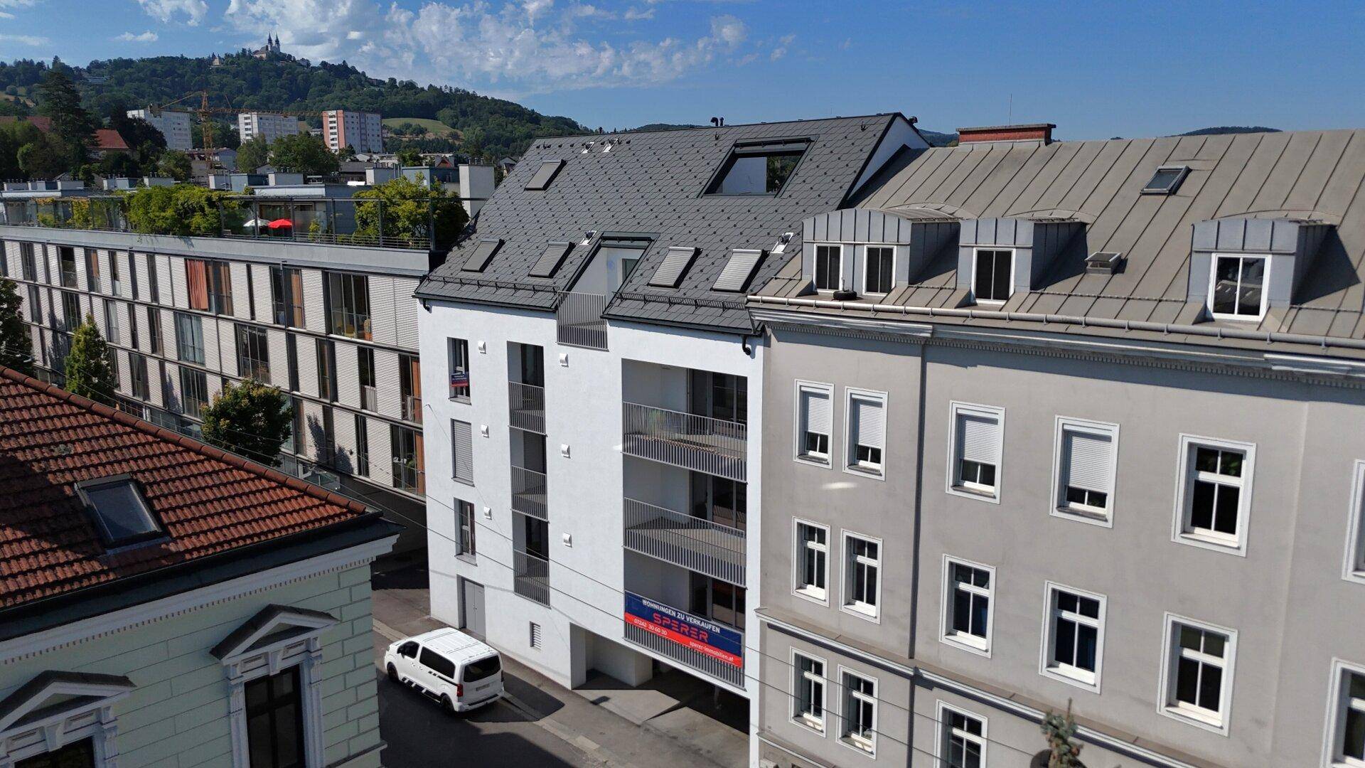 Blick auf ein modernes Wohngebäude mit Balkonen und ein angrenzendes älteres Haus in einer städtischen Umgebung.