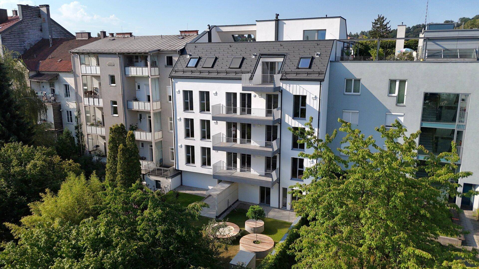 Rückansicht eines modernen Wohngebäudes mit Balkonen und einem gestalteten Gartenbereich mit Sitzgelegenheiten.