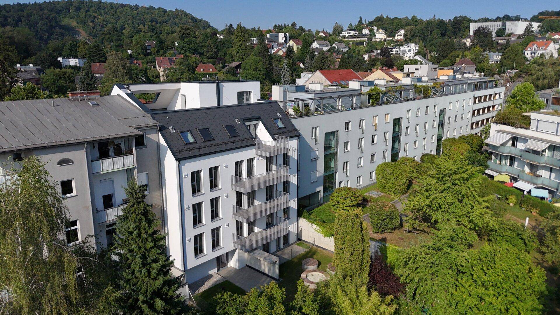 Panoramablick auf eine moderne Wohnanlage mit verschiedenen Gebäuden, Dachterrassen und grüner Umgebung.