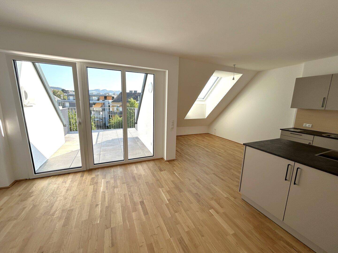 Heller, offener Wohnbereich mit Holzboden, Dachschrägen, Dachfenster und Zugang zu einem kleinen Balkon.