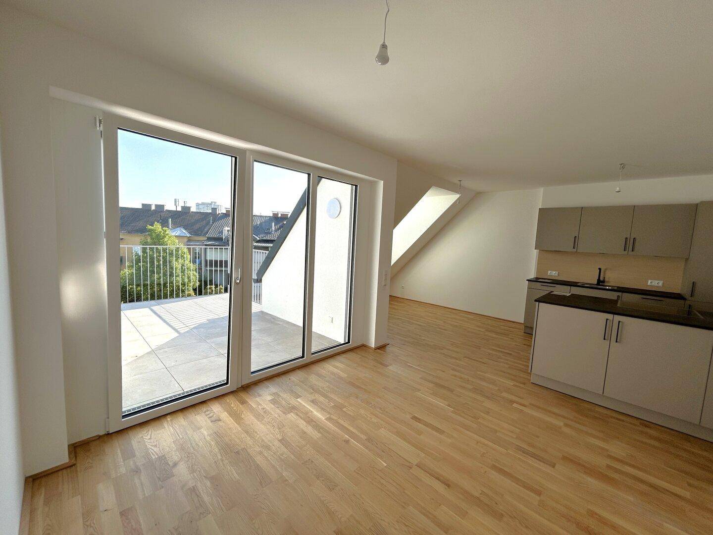 Lichtdurchfluteter Wohnbereich mit Eichenparkett, Zugang zum Balkon und Dachfenster.