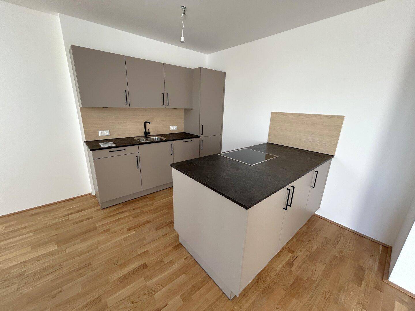 Moderne Einbauküche mit grauen Schränken, dunkler Arbeitsplatte und Kochinsel.