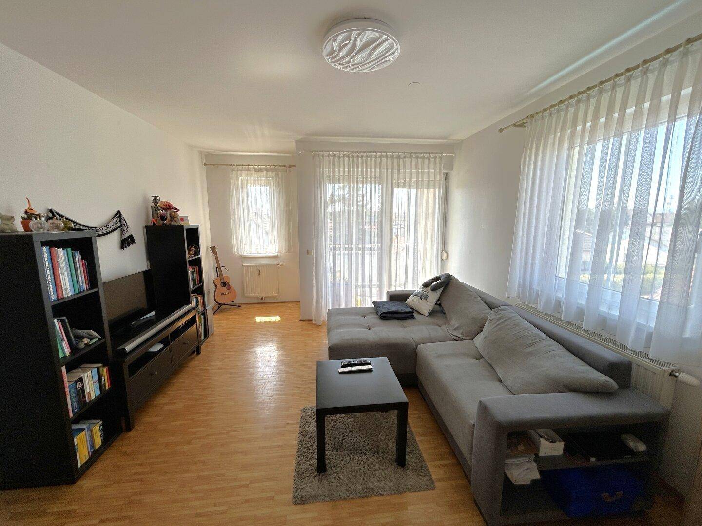Helles Wohnzimmer mit Laminatboden, großem Ecksofa und Zugang zum sonnigen Balkon.