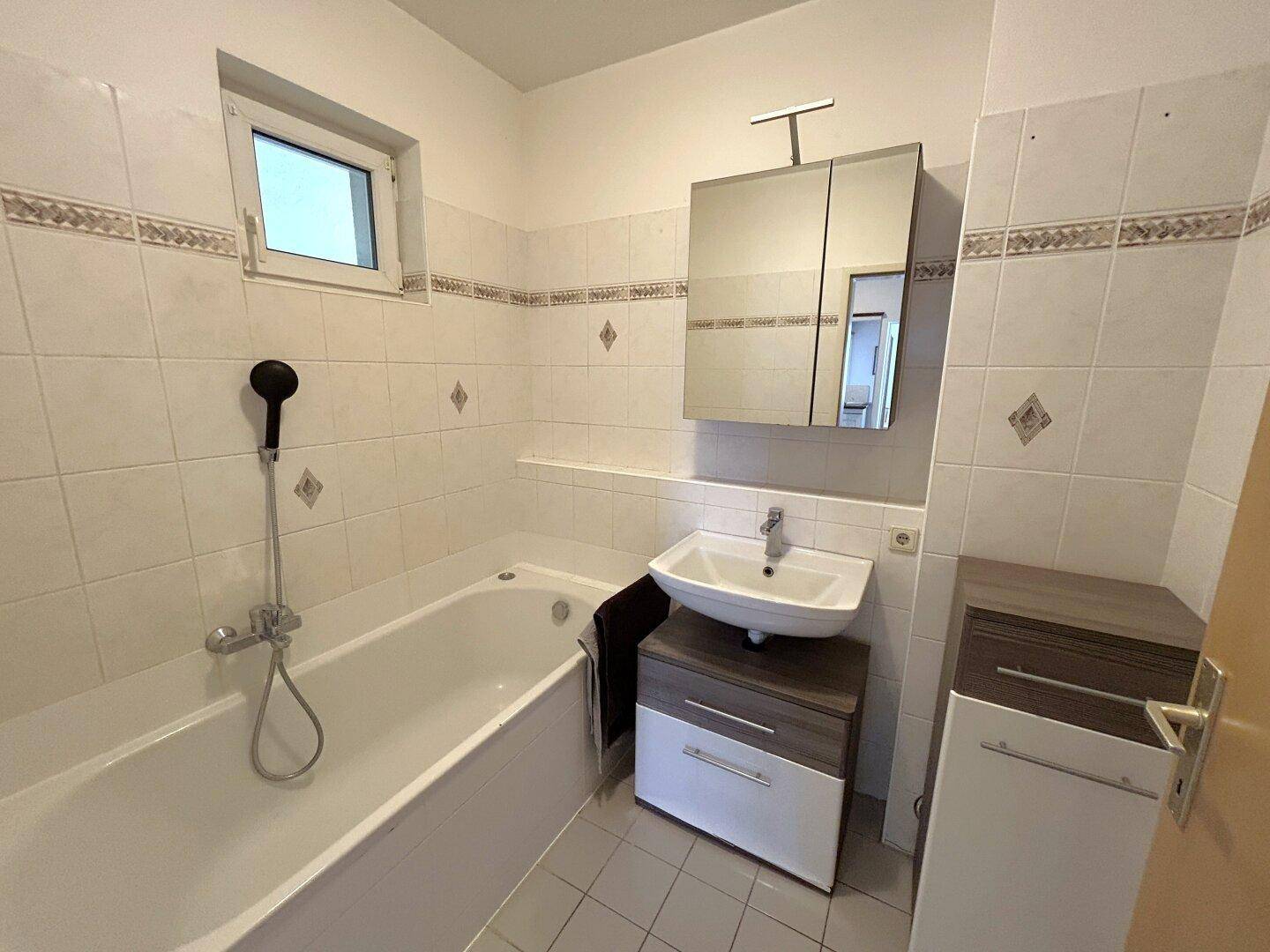 Badezimmer mit Badewanne, Waschbecken, Spiegelschrank und Fenster für natürliches Tageslicht.