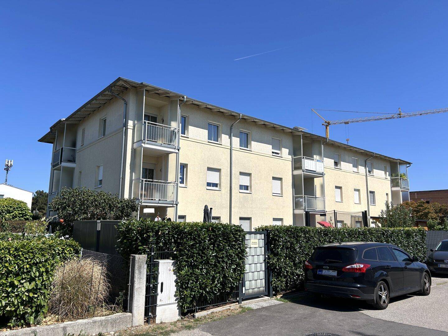 Außenansicht des Mehrfamilienhauses mit Balkonen und umgebender Grünfläche unter blauem Himmel.
