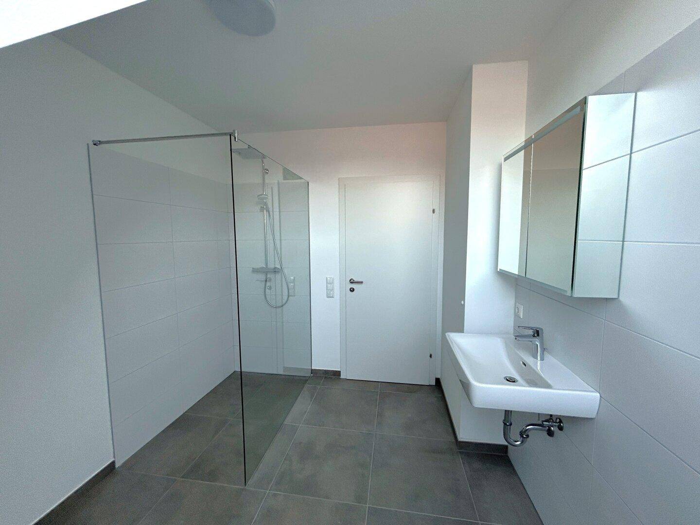 Modernes Badezimmer mit ebenerdiger Glasdusche, Einzelwaschbecken und Spiegelschrank, hell gefliest.