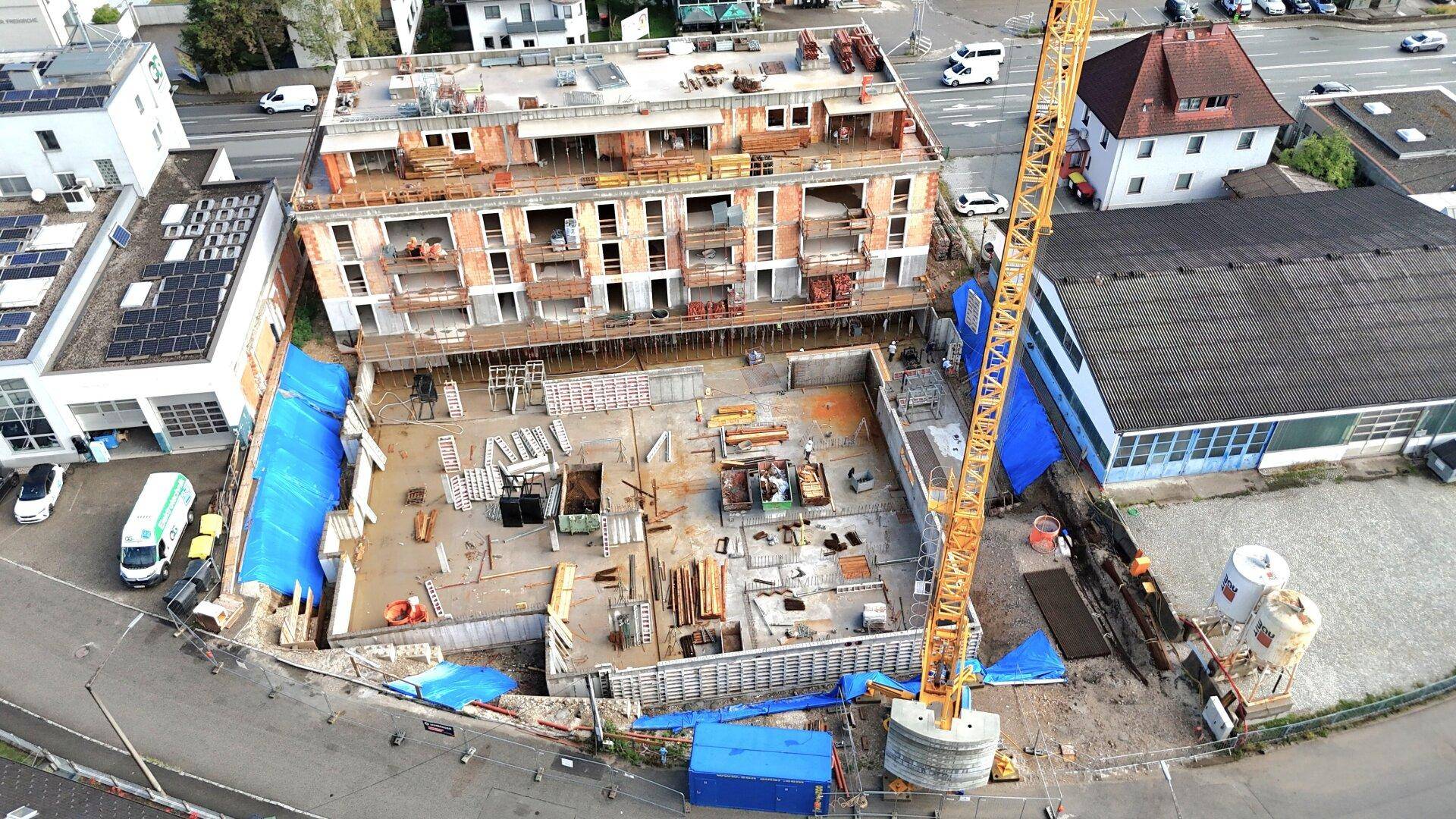 Vogelperspektive auf eine Baustelle mit einem im Bau befindlichen Gebäude und einem großen Kran.
