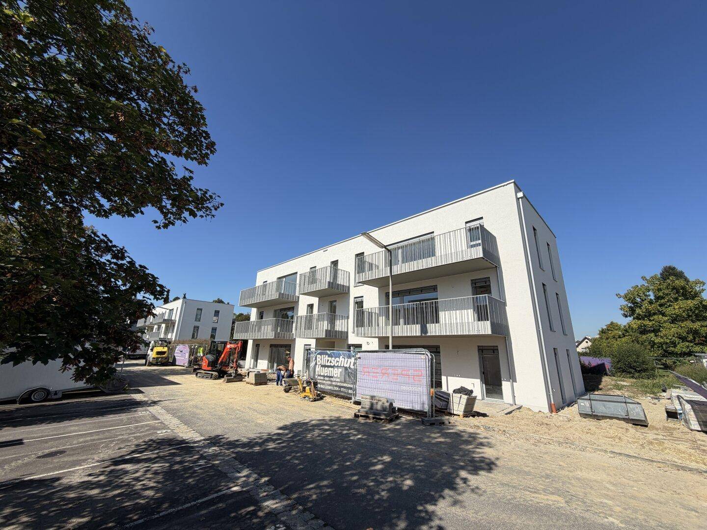 Neubau-Wohngebäude mit modernen Balkonen und Baustellenaktivitäten im Vordergrund bei Sonnenschein.