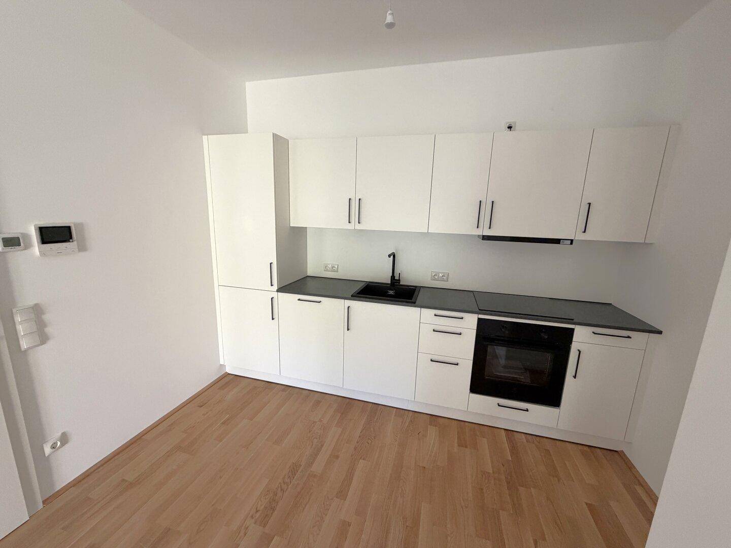 Moderne Einbauküche in Weiß mit dunkler Arbeitsplatte, integriertem Backofen und Holzfußboden.