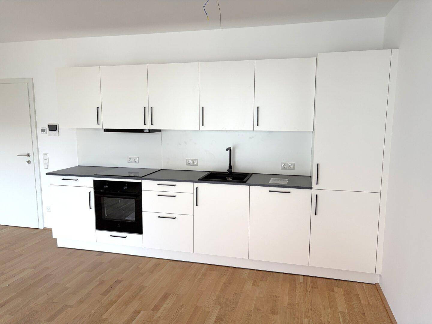 Moderne, weiße Einbauküche mit integriertem Backofen und Induktionskochfeld in neuwertigem Zustand.