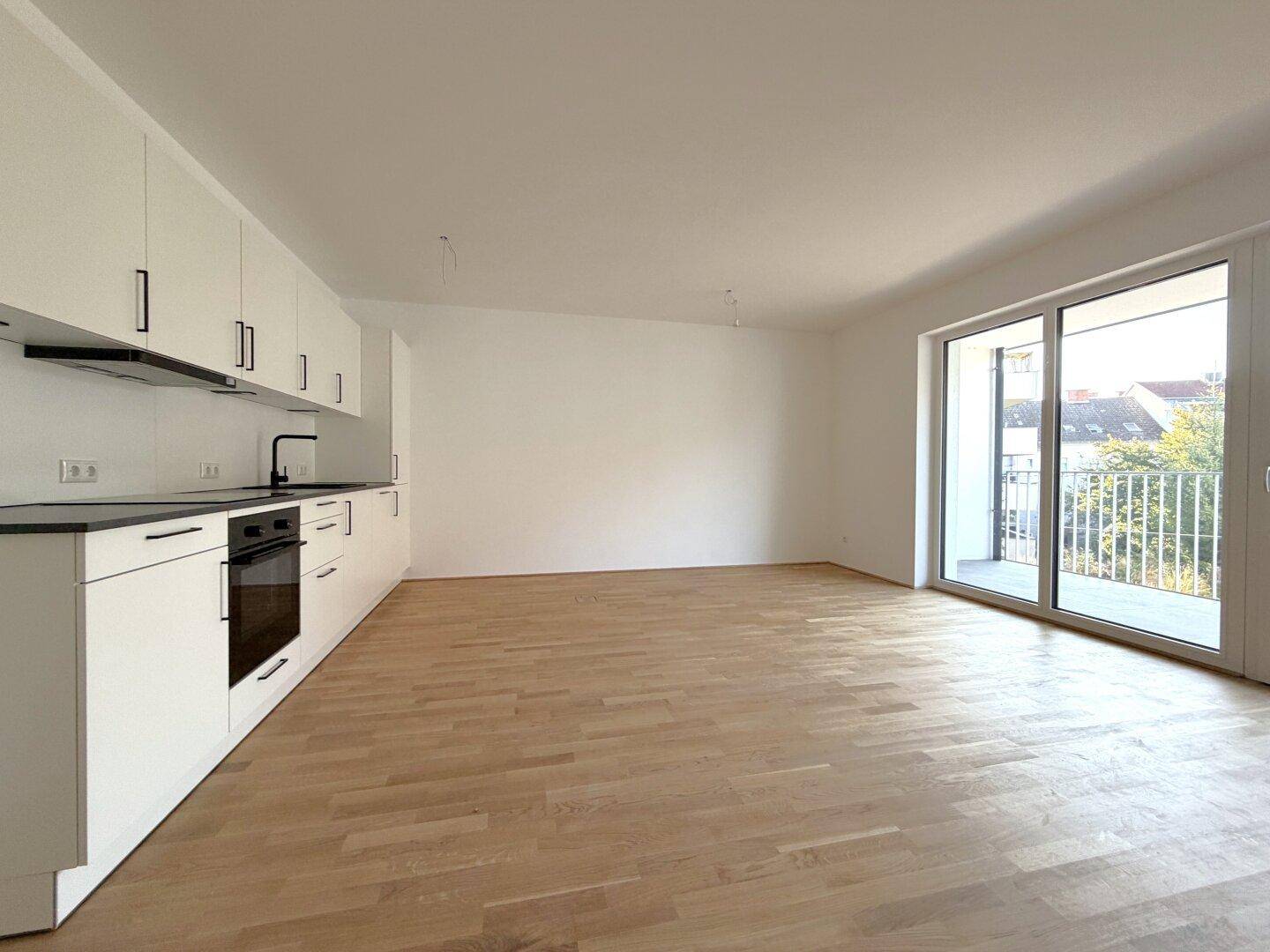 Heller, offener Wohn-Essbereich mit moderner Einbauküche und Zugang zum Balkon.