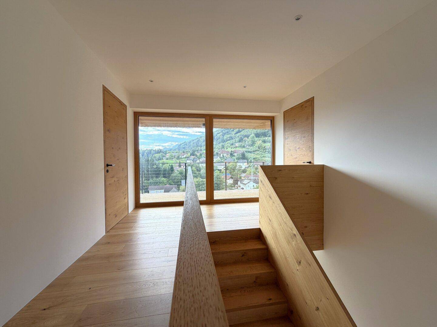 Heller Flur mit Holztreppe, Holzboden und großen Fenstern mit Panoramablick.