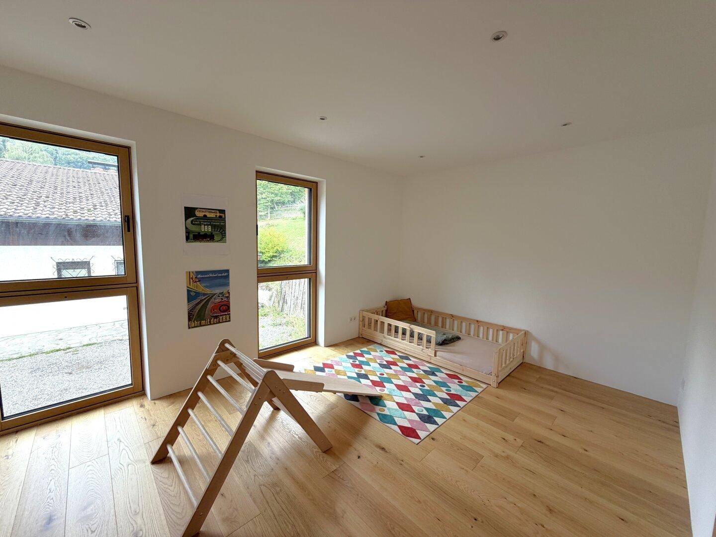 Kinderzimmer mit Holzboden, großen Fenstern und kindgerechter Einrichtung.