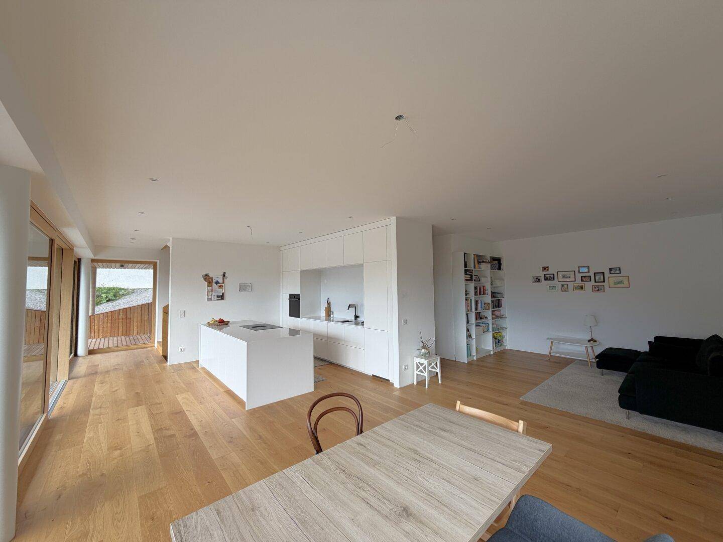 Heller, offener Wohn-Essbereich mit moderner Küche, Holzboden und großen Fenstern.
