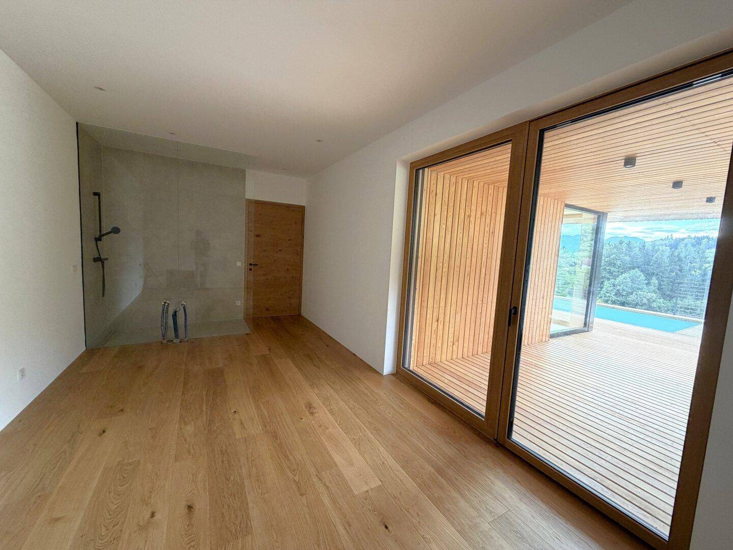 Geräumiges Badezimmer mit begehbarer Dusche, Holzboden und Zugang zur Terrasse.