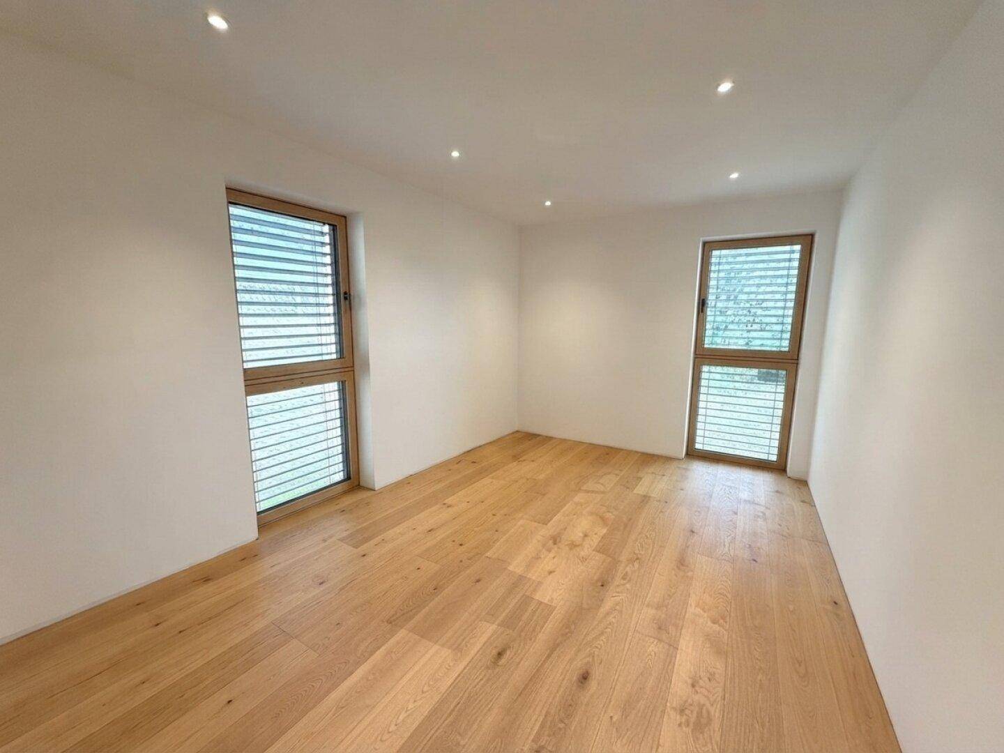 Helles Zimmer mit Holzboden und zwei Fenstern, ideal als Schlaf- oder Arbeitszimmer.