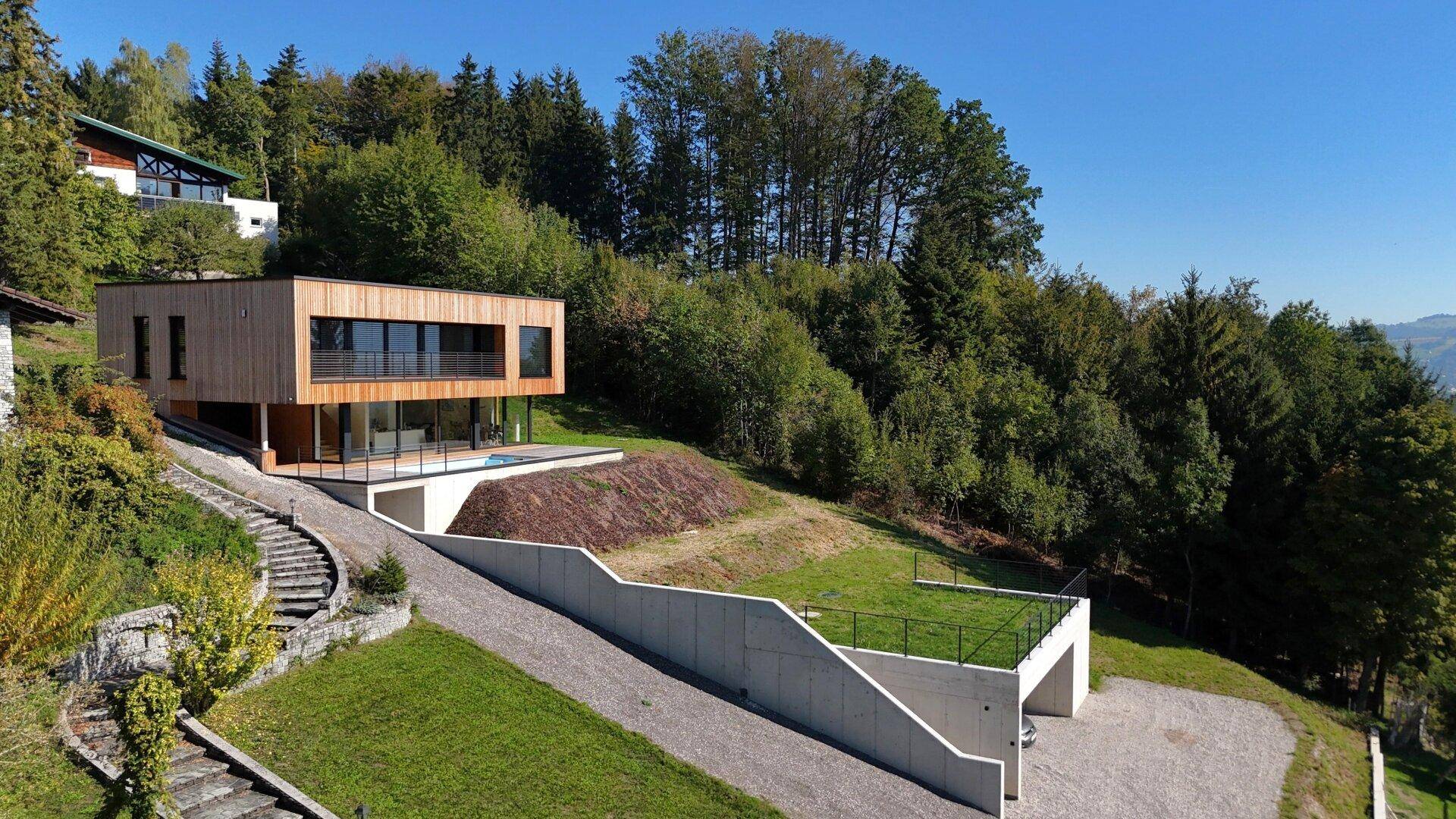 Architektonisch ansprechendes Haus in Hanglage mit Holzfassade und weitem Blick ins Grüne.