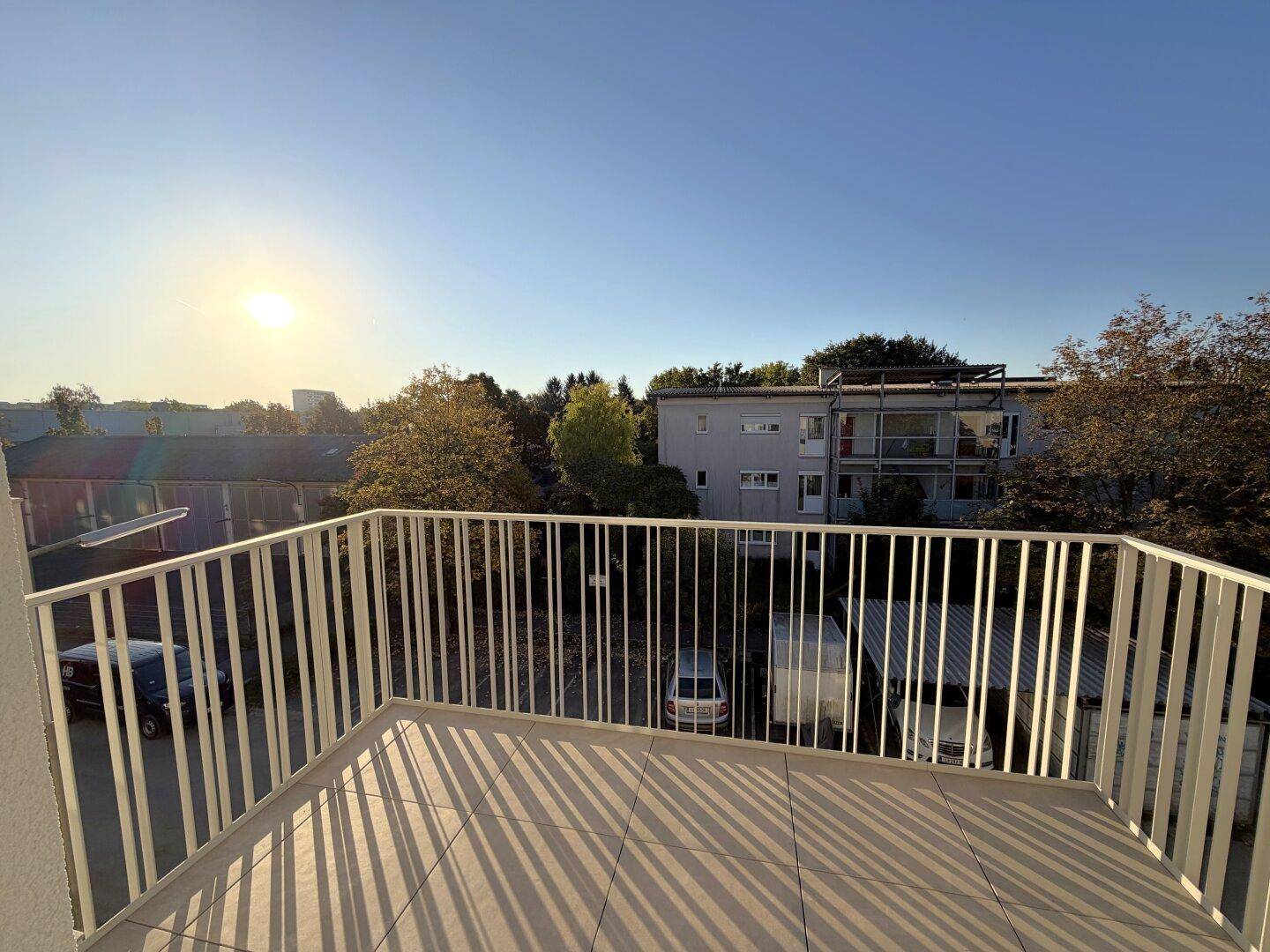 Geräumiger Balkon mit Fliesenboden und Blick auf die Umgebung bei Sonnenuntergang.