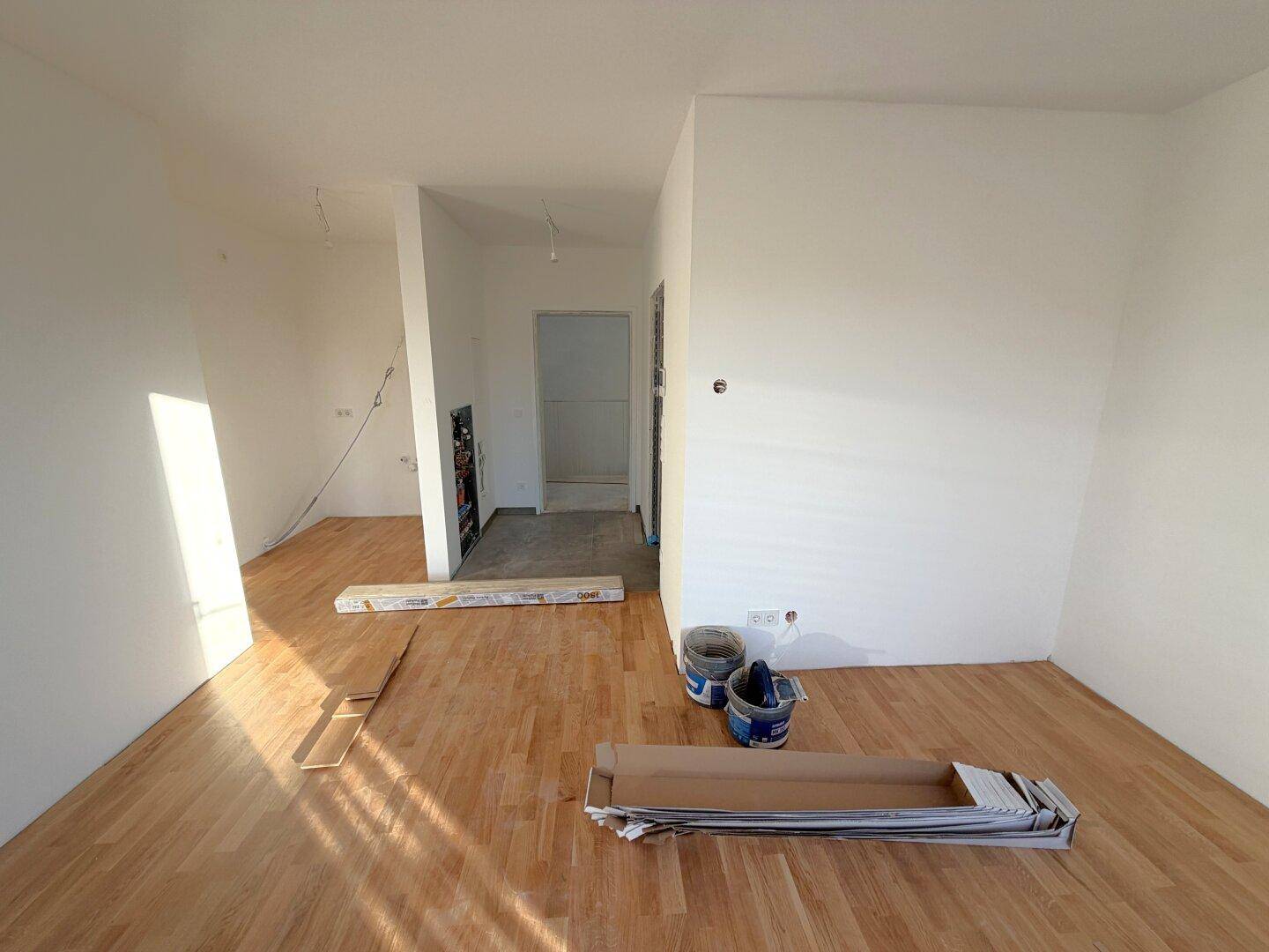 Unfertiges Zimmer mit Holzboden und weißen Wänden, bereit für den weiteren Ausbau.