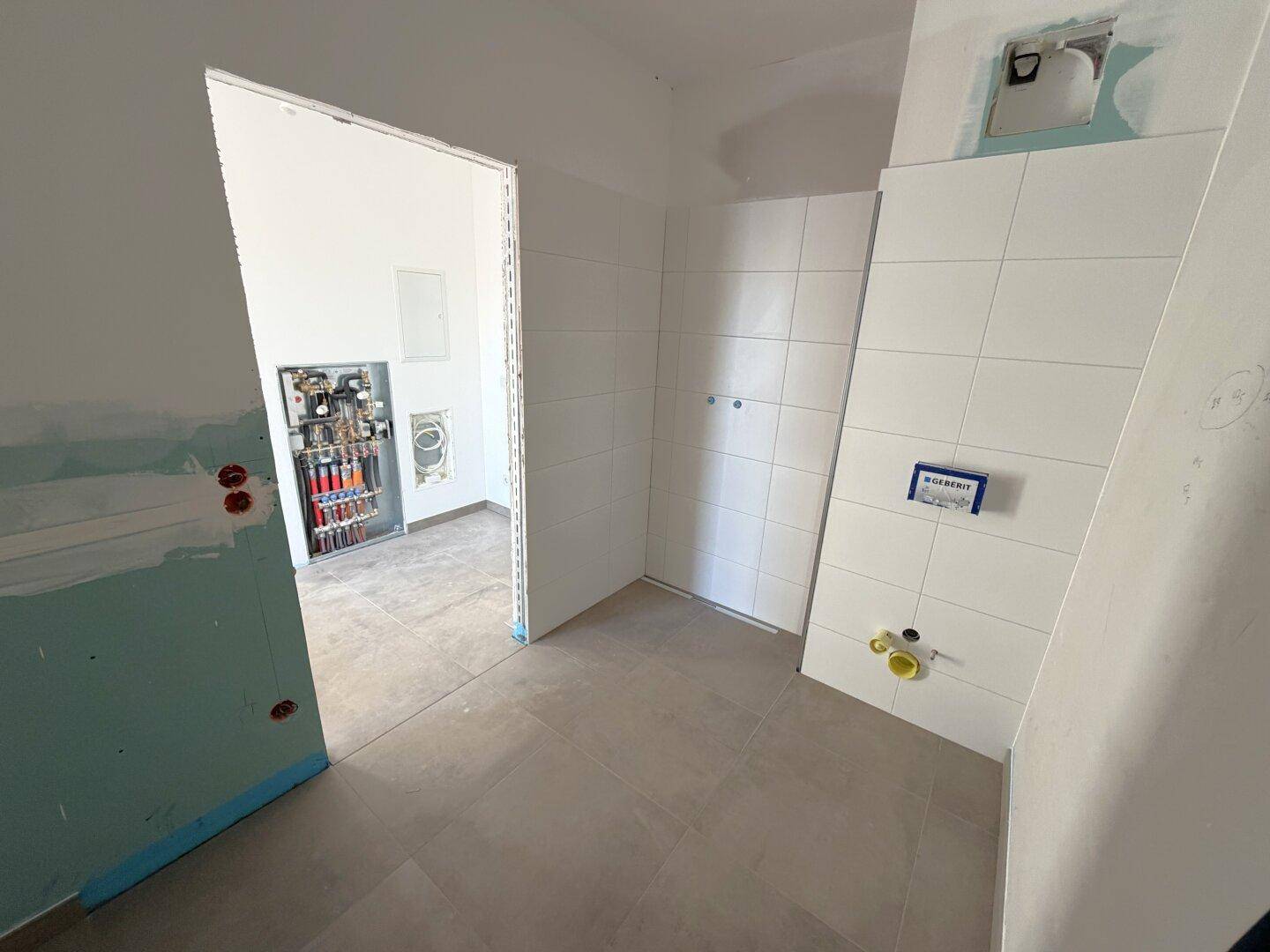 Unfertiges Badezimmer mit weißen Fliesen und sichtbaren Installationen, bereit für den Endausbau.