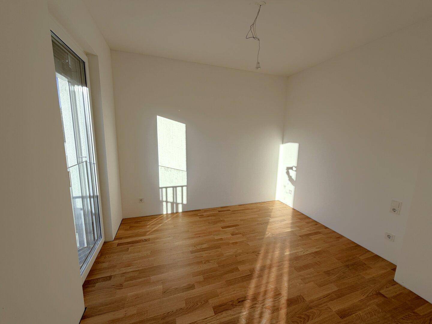 Helles Schlafzimmer mit Holzboden und Zugang zu einem französischen Balkon, sonnendurchflutet.